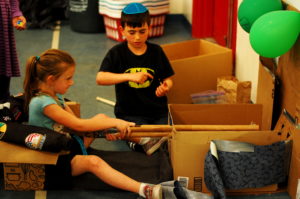 A student teaches another student how to play his arcade game.