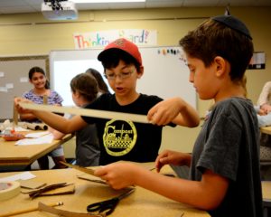 A student unrolls a roll of masking tape as he starts work on his sukkah design prototype.