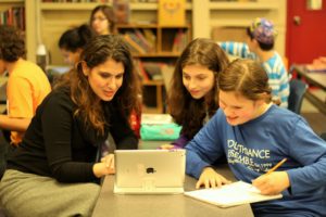 Lisa Schopf and two students are smiling and looking at something on a tablet computer.