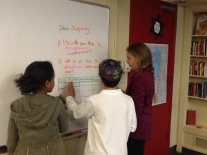 Three students are writing on a whiteboard in a classroom.