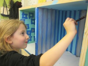 A student paints bookshelves in different shades of blue before they are installed in the South Campus Library.