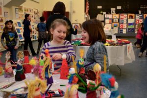 Two students explore tables of artwork in the Gottesman Auditorium.