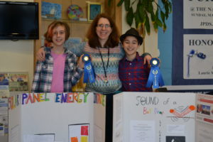 From left to right, STEM Fair winner Yael N., Science Specialist Elana Cohen, and STEM Fair Winner Gabriel B. pose with the students' project boards and blue ribbons.