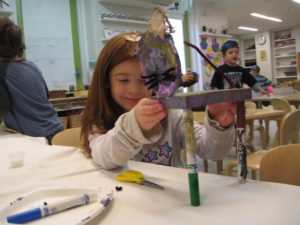 A girl balances a piece of artwork on two thin legs made out of repurposed markers.