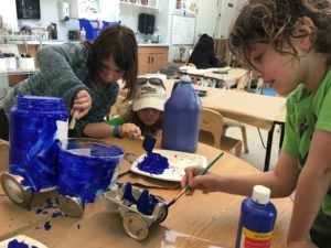 Two students work together to paint an object bright blue.