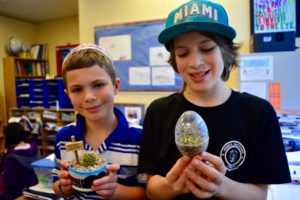 Two students hold up terrariums on "Bring a Plant to School Day."