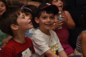 Two children smile as they watch the magician perform at the Summer Brunch.
