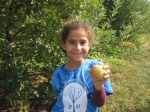 A South Campus student holds up an apple in the middle of an apple orchard.