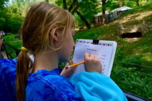 A student takes notes in Hebrew outside of an animal enclosure.