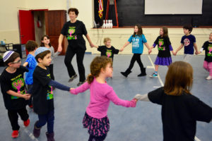 Children dance holding hands in a circle with Sharon Gelboin-Katz at the Rokdim B'Yachad Dance-a-Thon.