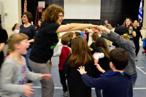 Head of School Naomi Reem helps form a bridge for students to dance through.