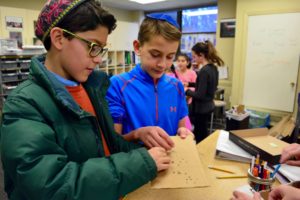 Fifth graders work in the design lab perforating cardboard sheets.