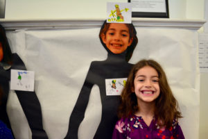 A student stands next to her self-portrait with adjectives.