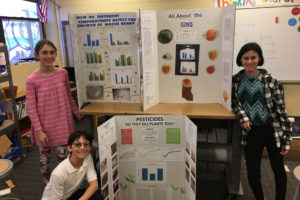 Lael, Emmett, and Ana pose for the camera with their Inquiry Project presentation boards.