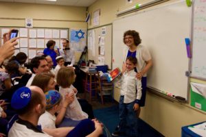 Head of School Naomi Reem presents a first grader with his new siddur (prayerbook).