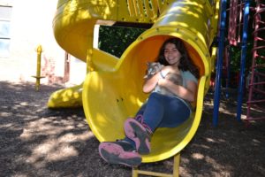 A student slides down the playground slide while holding her cat.