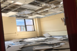 An empty classroom, ceiling tiles scattered across the floor.