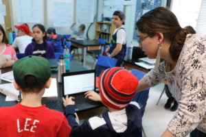 Judaic Studies teacher Devora Hornstein works with fifth grade students on laptops.