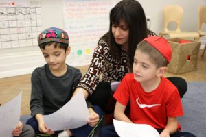 First grade Hebrew Teacher and Hebrew Instructional Leader for Early Childhood Vered Goldstein helps two students with Hebrew worksheets.