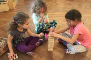 Three Kindergarten students play Jenga as part of their research on games.