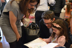 A student reads her homemade book with her parents at the Pre-K Bayit Patuach (Open House).