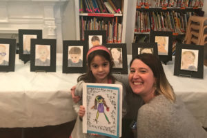 A pre-kindergarten student poses with her mother in front of her "sad" portrait.