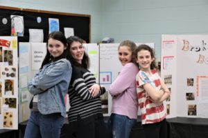 Sixth graders pose in front of their Inquiry Project boards.