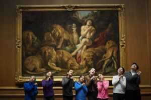 Sixth graders strike a pose mimicking Daniel in front of the painting "Daniel in the Lions' Den" by Rubens.